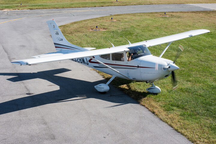 A small white propeller plane is positioned half on the runway and half on the grass.