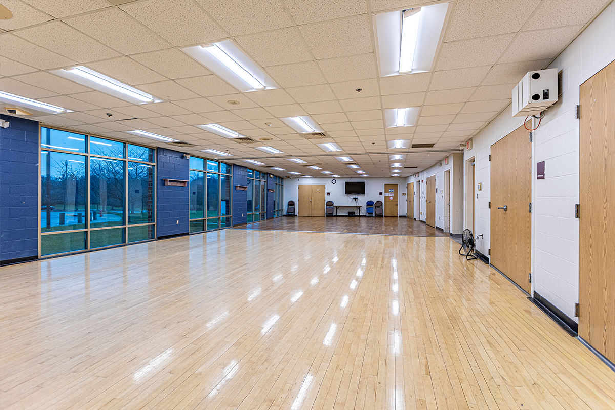 A large, multipurpose room with a hardwood floor and one wall with floor-to-ceiling windows.