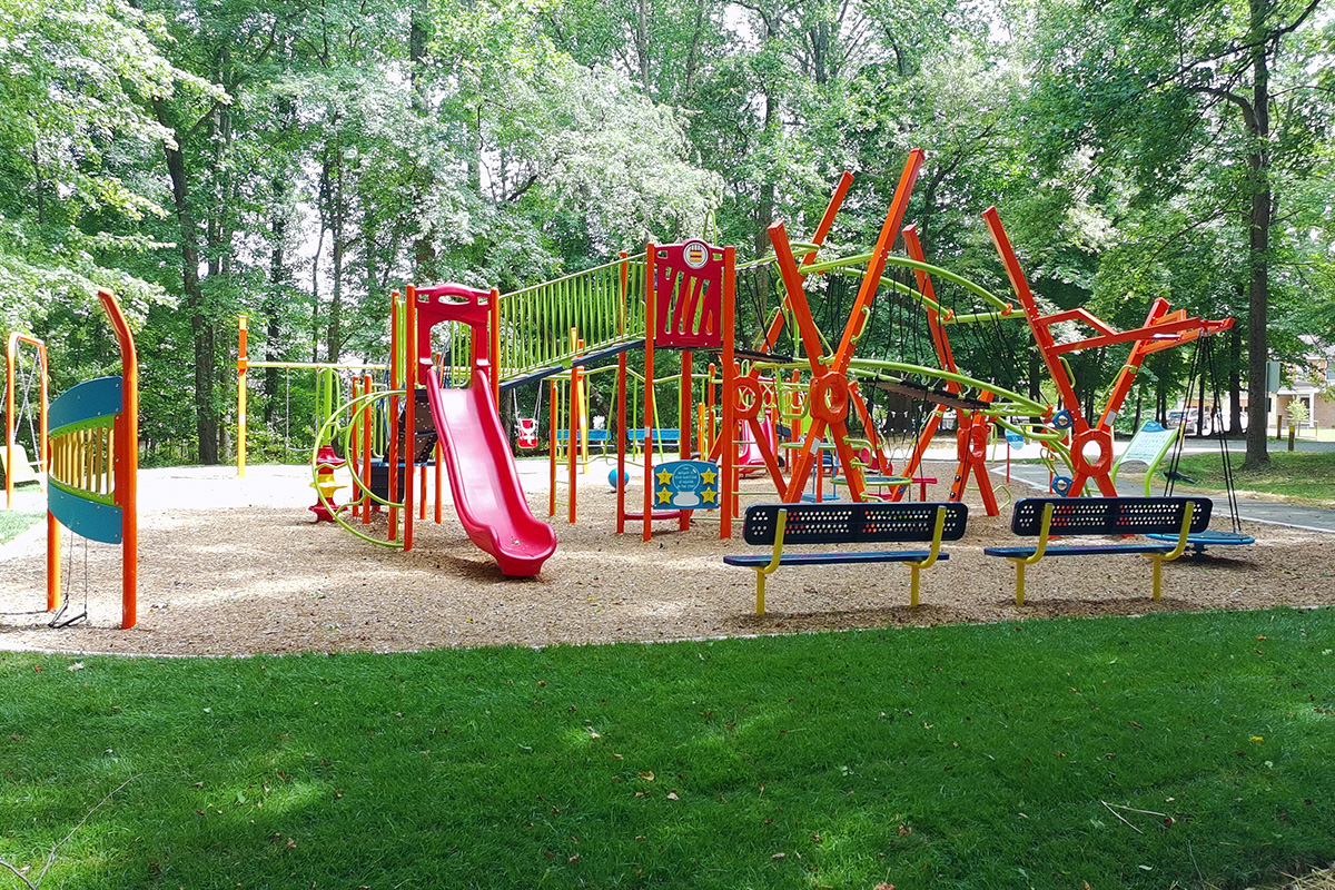 Wide view of the playground's climbing and active play features within a wooded park setting.
