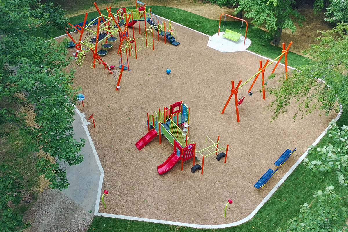 Aerial view of Willow Wood Playground showing age-specific play zones, climbing features, swings, accessible amenities, and gathering spaces within a wooded park setting.