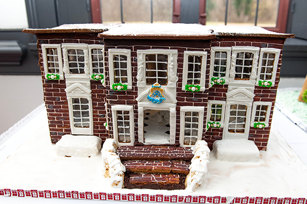 A beautiful flat-top roof, two-story dark brick gingerbread building. Complete with white frosting crown molding, and glazed sugar glass windows surrounded by gorgeous frosting trim work. A beautiful gingerbread brickwork staircase leads up to the decorated front door.