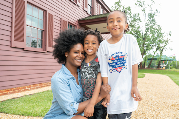 Adult and two children pose together outdoors beside a historic building.