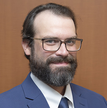 Headshot of a smiling man wearing glasses and a blue suit and tie.