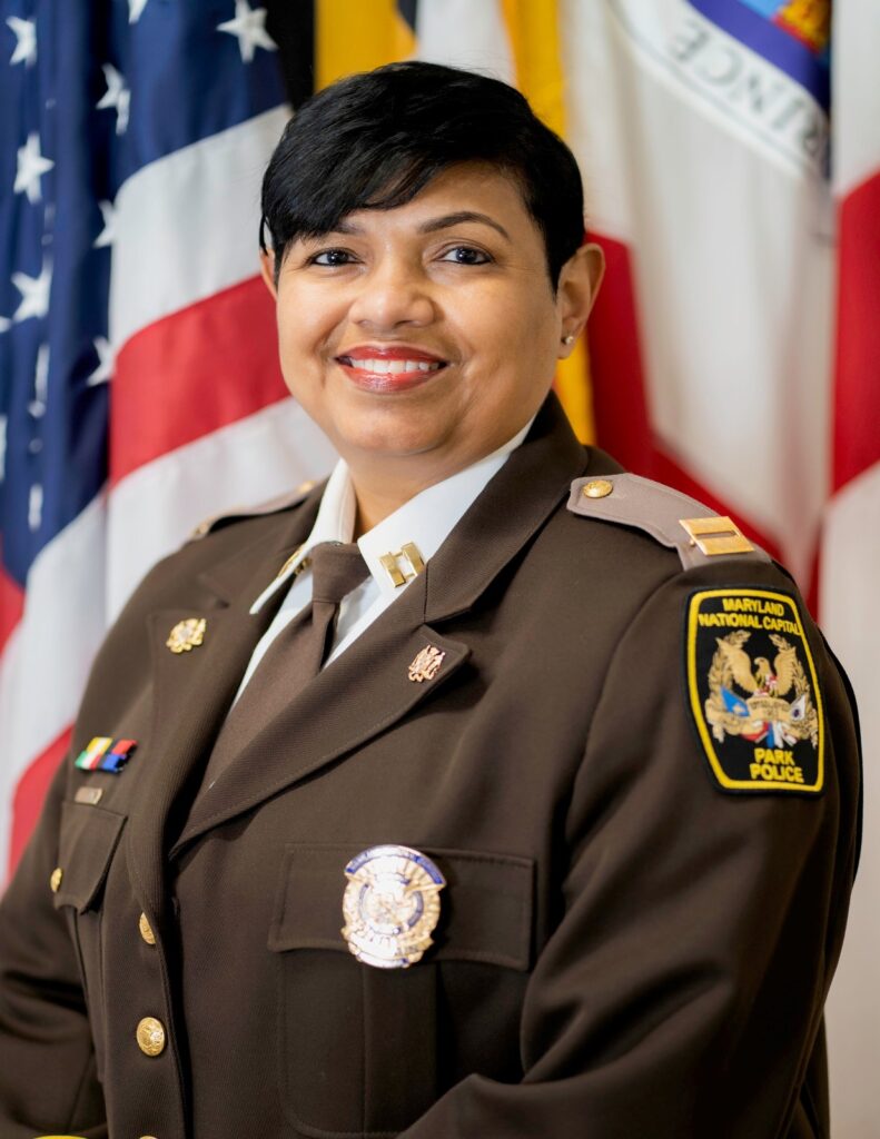 Uniformed park police official in dress uniform, photographed before American, Maryland, and Prince George's County flags.