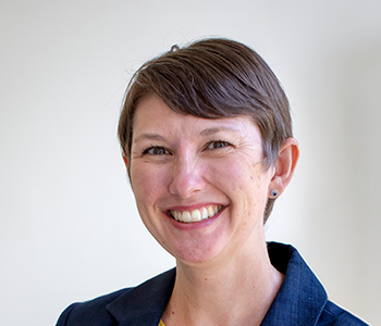 Headshot of a smiling woman with short hair, wearing a blue jacket.