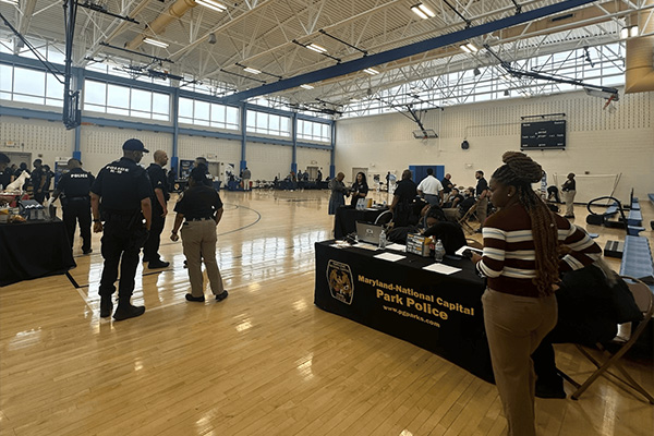 Community members walk to booths in a gymnasium to learn about Park Police from Officers.