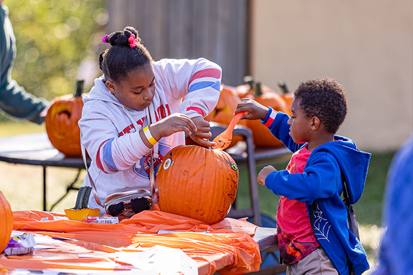 Two young people scoop the seeds out of a decorated pumpkin.