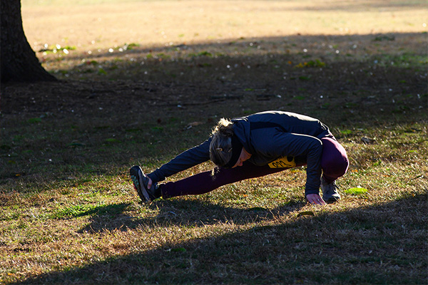 A runner performs a leg stretch in the grass, dramatically lit by a shaft of sunlight.